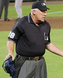 Photograph of Larry Young as home plate umpire holding his mask in his right hand