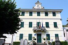 A color photo of a three story building with shuttered windows, three flags, and a clock tower.