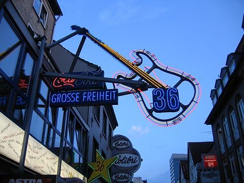 A street sign with a quitar lighted by neon light.