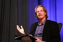 A seated Joel Christensen giving a lecture on Homer.