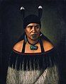 Image 31Hinepare of Ngāti Kahungunu, is wearing a traditional korowai cloak adorned with a black fringe border. The two huia feathers in her hair, indicate a chiefly lineage. She also wears a pounamu hei-tiki and earring, as well as a shark tooth (mako) earring. The moko-kauae (chin-tattoo) is often based on one's role in the iwi. (from Culture of New Zealand)