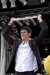 Gómez, in a suitcoat, lifts the Bundesliga trophy above his head