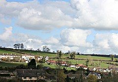 Several houses, many with white walls and red roofs nestling in a green valley with occasional trees.