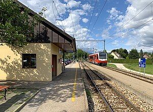 Yellow station building next to a railway line with a red and white train in the background