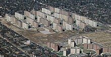 An aerial view of many large apartment blocks in a grassy expanse, surrounded by dense suburbs