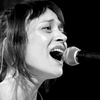 A black and white headshot of Fiona Apple singing into a microphone