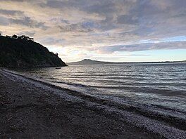 A beach during early morning, with an island on the horizon beneath a cloudy sky