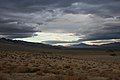 A landscape shot of a long, dry valley. The sky is partially clouded over but blue sky breaks through in patches. It is a showcase of Nevada's natural beauty.