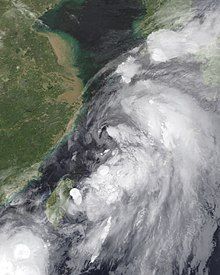 A photograph of a large and disorganized tropical storm off the east coast of China; the system's structure consists of multiple amorphous blobs of convection, with lower clouds making a circulation evident.