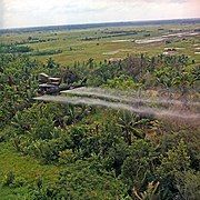 A UH-1D helicopter from the 336th Aviation Company sprays a defoliation agent over farmland in the Mekong Delta.