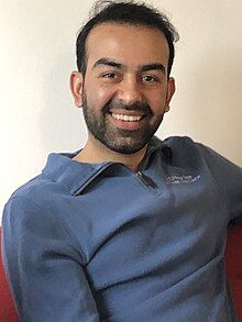 Portrait of a man from the waist up, wearing a blue shirt.