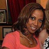 A woman wearing gold earrings and two gold necklaces along with a peach-colored shirt.