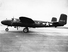 Black and white photo of an early bomber parked perpendicular to the camera, facing left, rearward of the wing is a star in front of horizontal stripes.