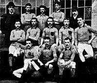 A group of thirteen men, eleven in association football attire typical of the late nineteenth century and two in suits and bowler hats.