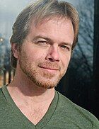 A white man in a green V-neck t-shirt.