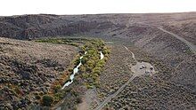 Drone image of the West Little Owyhee River at Anderson crossing. This image is from September, so the water is very low. Lush green plants flank the river for 10-20 feet on each side, then becomes sagebrush.