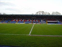 Bury F.C.'s blue stadium seated stand covered in red, white and black F.C. United banners.