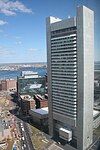 Aerial view of a tall, narrow, concrete skyscraper; the building's design somewhat resembles that of a washboard, with uninterrupted horizontal rows of windows protruding slightly outward from two of the building's four sides