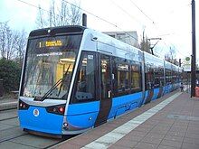 Tram at tram stop. The lower section of the tram sides slope inwards so the base fits next to the platform but the upper section is wider