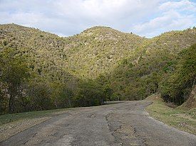 photo of a paved road, with crumbling pavement, and 3 hills in the distance