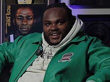 Tee Grizzley in 2024 in an interview sitting next to a vinyl of Mos Def’s Black on Both Sides album.