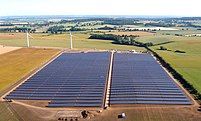 Aerial view of a solar farm with part of a wind farm in the background