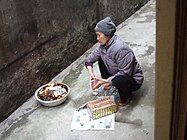 Woman burning joss papers in front of her house in Hanoi after offering food to her ancestors