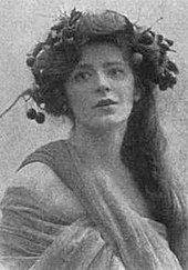 Head and shoulders of a woman with long dark hair, wearing a draped costume and an ivy wreath in her hair