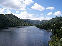 A circular, dark blue lake surrounded by numerous tree-covered hills.