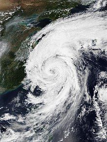 A photograph of a typhoon over the East China Sea; the convection is generally lopsided, being thick on the system's northern side and thin to its south, but the overall cloud pattern is well-organized and tightly wound, with an eye visible near the center.