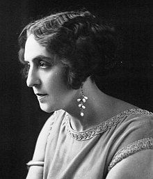 A white woman in near-profile, with wavy cropped hair, wearing beaded drop earrings.