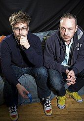 Colour photograph of Felix Buxton and Simon Ratcliffe of Basement Jaxx sitting on a sofa.