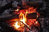 Gas and liquid aerosol are still burning and glowing as they stream away from the solid wood in this campfire.