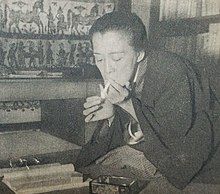 A Japanese woman bent forward, seated indoors, lighting a cigarette