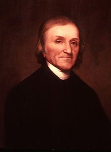 Half-length portrait of elderly man with wispy brown hair. He is wearing a black jacket and a white shirt.