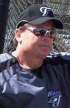 Man in sunglasses and baseball uniform leaning against a fence