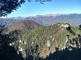 A mountain with trees and greenery, and more mountains in the background.