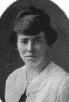 A white woman with dark hair in an updo, wearing a white blouse