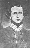 Black and white photo shows a clean-shaven, young man dressed in a gray military uniform with a bright-colored collar.