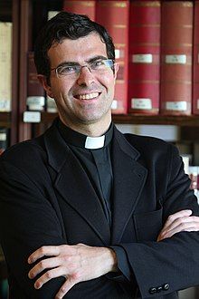 colour image of Pablo Blanco (aged 46) wearing his black priestly clothes in a library.