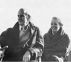 Bald man in overcoat next to woman wrapped in a blanket