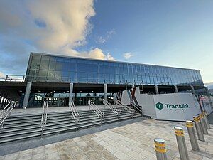 An image of a large train station with large glass windows and a Translink logo on a wall beside a set of stairs