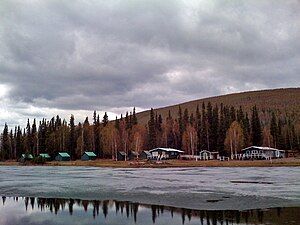 Scattered cabins are seen behind a lake with ice floating on its surface