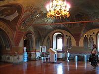 Side view of a narthex in an Eastern Orthodox temple. In the center is an analogion at which the priest hears confessions, to the right of that is a silver baptismal font and vessels for dispensing holy water. The main hall is to the left (Pechersky Ascension Monastery, Nizhny Novgorod).