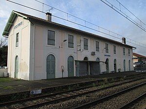 A long, 2-floored building with an array of doors leading up to a platform parallel to train tracks.