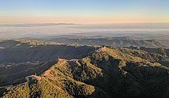 Loma Prieta (the peak just right of center) and other nearby peaks are decorated with television broadcast towers and other communication towers, serving the Santa Clara Valley. Fog-shrouded Monterey Bay and the Monterey peninsula are visible in the background in this late-afternoon approach to San José International Airport.