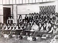 Black-and-white photo of Saddam Hussein, in a suit, with a group of women students