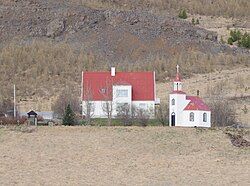 A church and a farm house with mountainous land rising up behind both