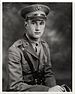 Head and torso of a white man sitting with his right arm resting on something in front of him. He is wearing a military uniform with a wide belt, a strap diagonally across the chest, and a peaked cap.