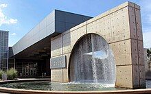 An image of the fountain in front of the main entrance. The design is a circle inside of a square with water falling down from the top of the circle into a pool.